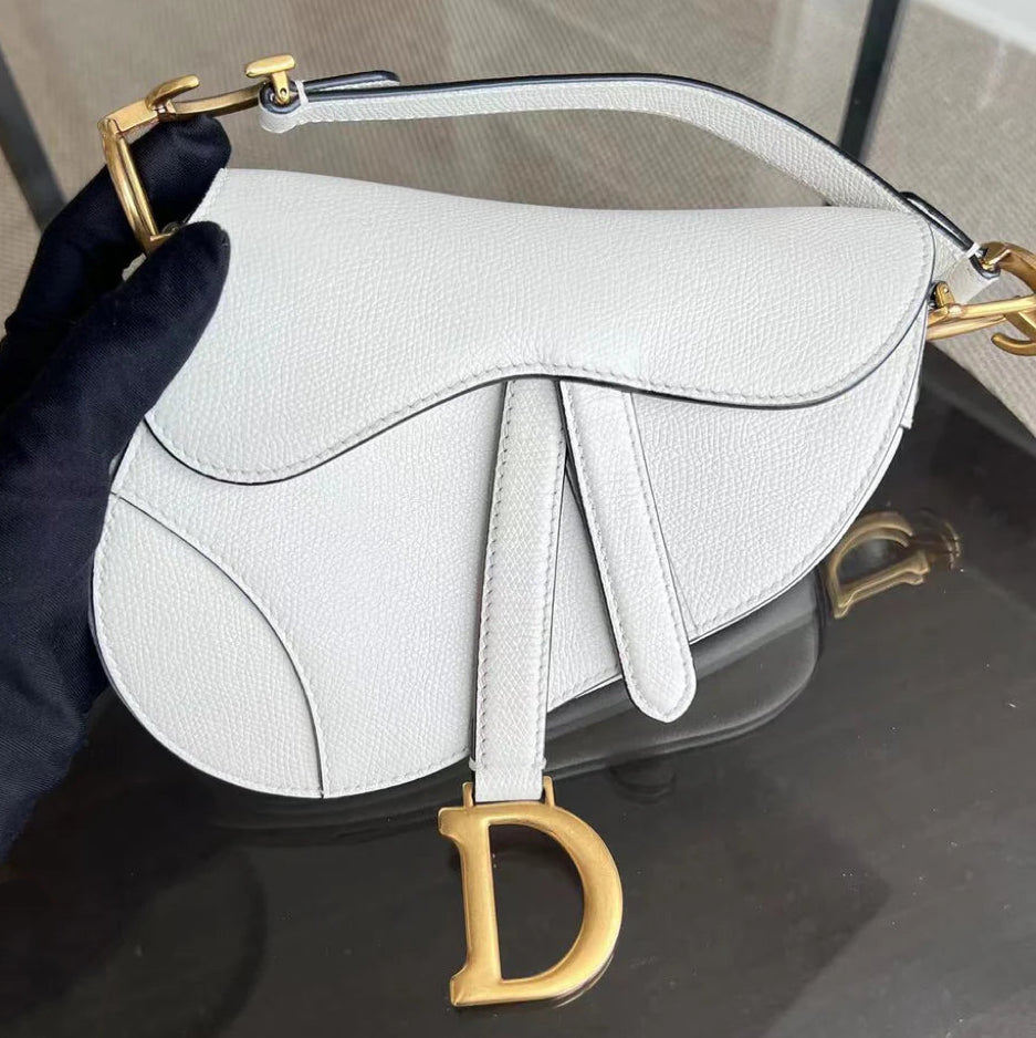 Kovancy Saddle Small 21 cm en cuir caviar blanc avec bandoulière et finitions dorées.