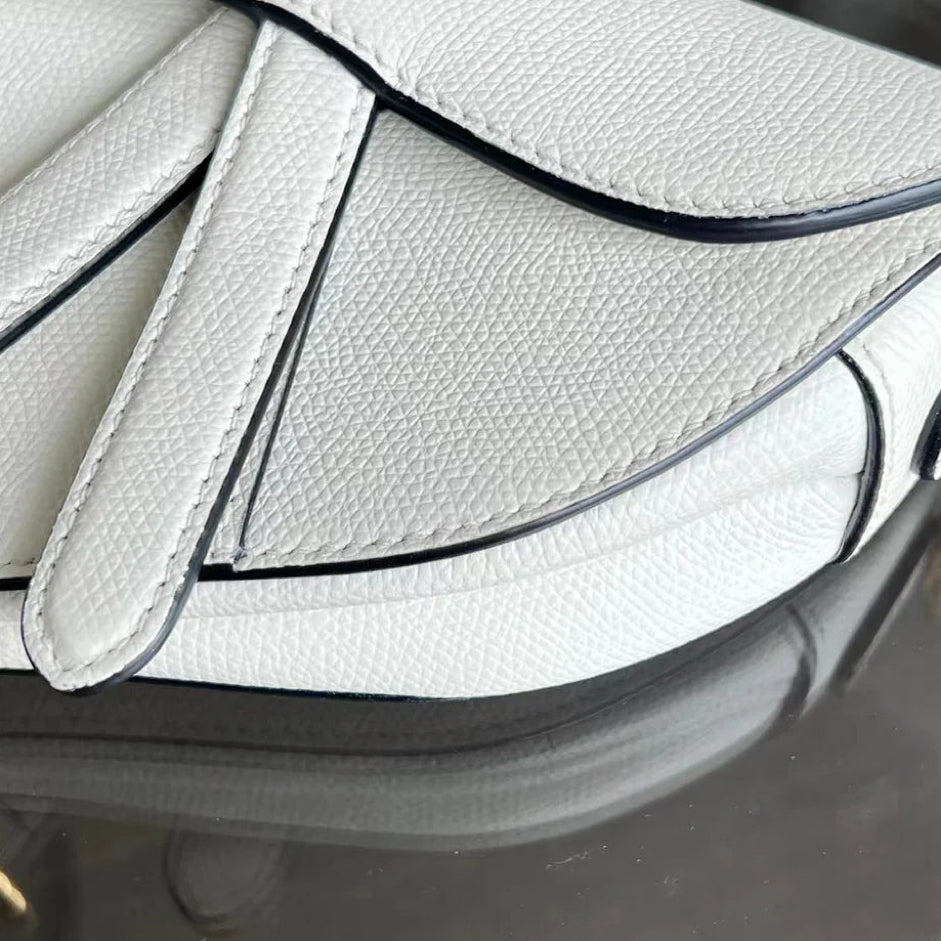 Kovancy Saddle Small 21 cm en cuir caviar blanc avec bandoulière et finitions dorées.